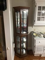 Full view of tall wooden curio cabinet with glass doors showing upper and lower display sections, wooden frame, and mirrored back inside.
