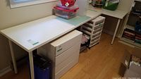 Wider view of the two-piece white desk set, including a larger and smaller desk placed in an L shape. Various items on the surface not included in sale.