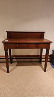 Front view of the vintage wooden desk showing the single drawer, turned legs, and raised back panel.