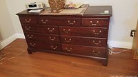 Front view of wooden dresser showing seven drawers and brass handles, items on top not included.