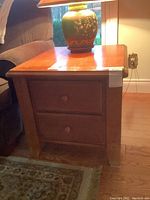 Front view of oak end table with two drawers and wooden knobs with a lamp on top.
