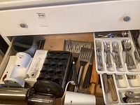 Drawer with various kitchen utensils including Herb'N Serve chopper, Pampered Chef decorator bottle set, coffee grinder, rolling pin, and flatware trays.