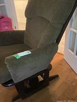 Close view of right armrest and base showing dark wood glider frame and olive green cushion