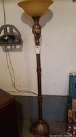 Full view of the floor lamp showing the entire height, bronze-colored ornate base, and amber glass shade.
