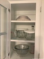 Shelves inside a cabinet holding nesting glass mixing bowls with plastic lids, a glass measuring cup, and a plastic measuring cup.