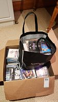 Photo showing a cardboard box filled with multiple music CDs and a black reusable tote bag on top holding more CDs