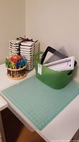 Overview of lot on white desk: cutting mat, green storage bin with tools, stacked stamp pads, wooden scissor organizer with scissors