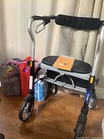 Front left side view of silver walker with padded black seat, foam backrest, hand brakes, and storage basket underneath.