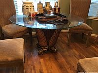 Full view of round glass top dining table with ornate carved wooden base surrounded by chairs