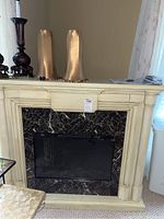 Front view of cream wood mantel surround with black faux marble insert and decorative items removed