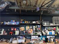Wide view of basement tool room wall with shelves holding various storage bins, containers, hardware products, and light bulbs.