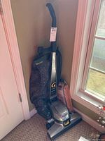 Full view of Kirby G Six Performance upright vacuum in corner with vacuum bag attached and extra bag in packaging beside it.