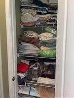 View of shelves with folded bed sheets, towels, bath mats, and other linens