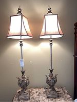 Pair of tall table lamps with metallic bases and crackle glass columns seen on a table, illuminated showing light diffusing through beige fabric shades.