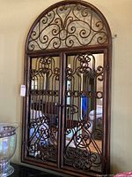 Front view of closed arched mirror with decorative metal scrollwork doors