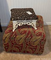 View of both the large paisley-patterned ottoman and the smaller decorative foot stool stacked on top, showing size and fabric details