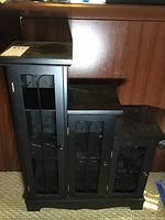 Black multi-level shelving unit with decorative metal scrollwork doors shown closed from front.