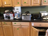 Wide shot of kitchen counter with multiple small appliances including toaster boxes and frying appliances