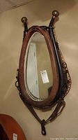Full oval horse collar wall mirror framed with brown leather and black metal, shown hanging vertically on wall.