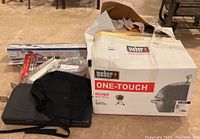 Weber One-Touch Silver grill in original box with black cover and grilling accessories laid out.