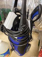 Full view of the AR Blue Clean 383 pressure washer with coiled hose and spray gun attached, detergent bottle holder on top.