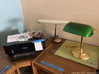 Photo showing Canon PIXMA iP4700 printer on wooden desk with ink cartridges and a manual on top, alongside two desk lamps (brass with green glass shade and brown lamp with cream shade).