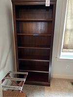 Front view of the tall cherry colored bookshelf showing all six shelves and the back panel with vertical planks.