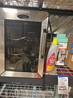 Cuisinart wine cellar with visible metal racks inside and glass door, situated on metal shelving with humidifier treatment bottle beside.