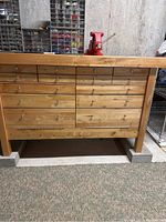 Front view of bench showing all drawers closed and red vise on top, natural wood finish, hardware storage bins in background