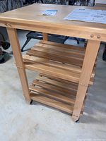 Wood shelf cart with two slatted lower shelves and solid top shelf, light wood finish, set on caster wheels.