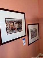 Two framed French themed prints hanging on a peach colored wall, showing full view of both pieces.