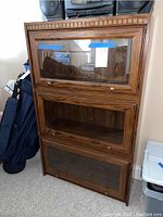 Front view of the oak veneer cabinet showing three separate glass pane doors covering individual shelves, decorative top trim, brass knobs.