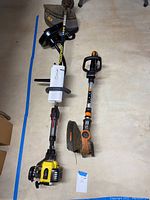 Wide shot of both trimmers laid out on a basement floor with manual for John Deere trimmer.