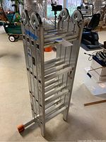 Folded ladder standing upright on concrete basement floor showing overall aluminum frame, hinge joints and orange foot caps.