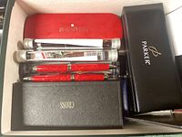 Photo showing luxury pens in Sheaffer, Parker, and Cross branded cases, including red and black pens in protective cases.