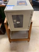 Front view of off-white Phoenix Dataguard 2000 safe on wooden stand showing key and lock mechanism through transparent door panel.