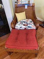 Front view of wood and rattan armchair with floral cushion, yellow pillow, and rust-colored ottoman cushion in front.