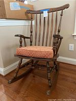 Front view of solid wood rocking chair with damask cushion on hardwood floor.