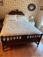 View of full Victorian wooden bed with cream bedding in floral wallpapered room