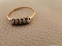Close-up photo of antique 14k yellow gold ring showing five pearls set in a row on a textured fabric background.
