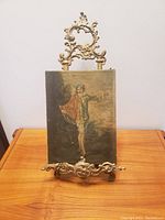 Image of the brass easel holding the vintage painting of a jester figure.