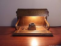 Photo showing antique hammered copper desk lamp illuminated on wooden surface.