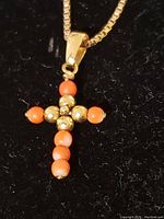 Front view of cross pendant showing alternating coral beads and polished gold spheres on black background