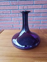 Front view of antique purple glass decanter showing bulbous base, tall neck, and stopper with metal ring.