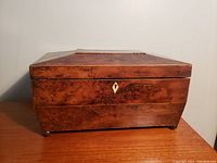 Front view of antique burl walnut tea caddy showing keyhole on hinged lid and burl wood grain.