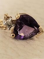 Close-up of pendant showing pear-shaped purple gemstone in three-prong setting with round clear stone accent