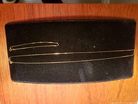 Two gold chains (necklace and bracelet) laid flat on black velvet pad