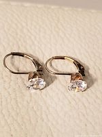 Pair of yellow gold lever-back earrings with clear round faceted stones shown on a white textured background.