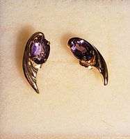 Top view of gold earrings showing purple gemstones and curved design.