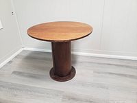 Full view of the round wooden vintage table showing the circular tabletop and cylindrical base.